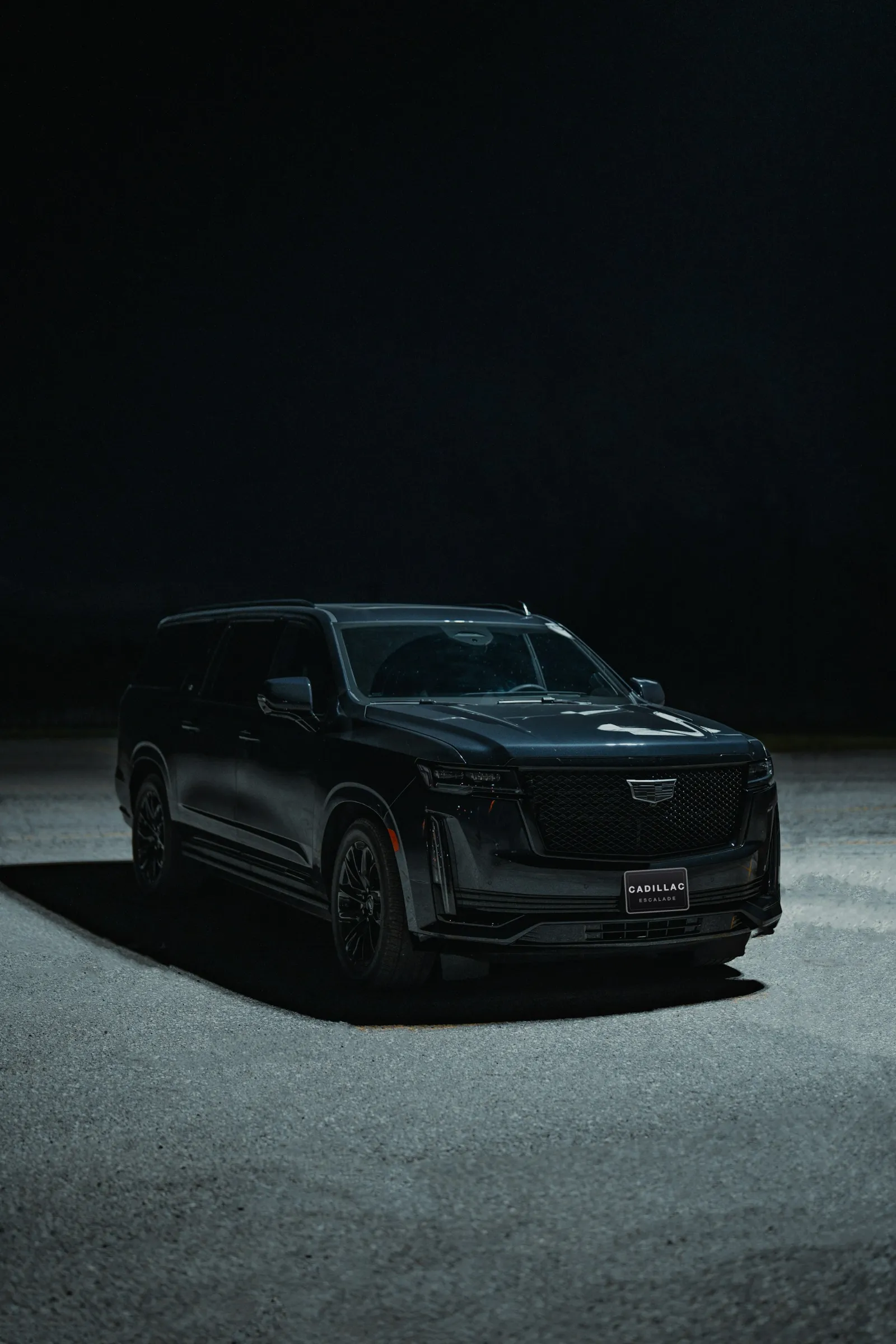 Black Cadillac Escalade under a spotlight at night