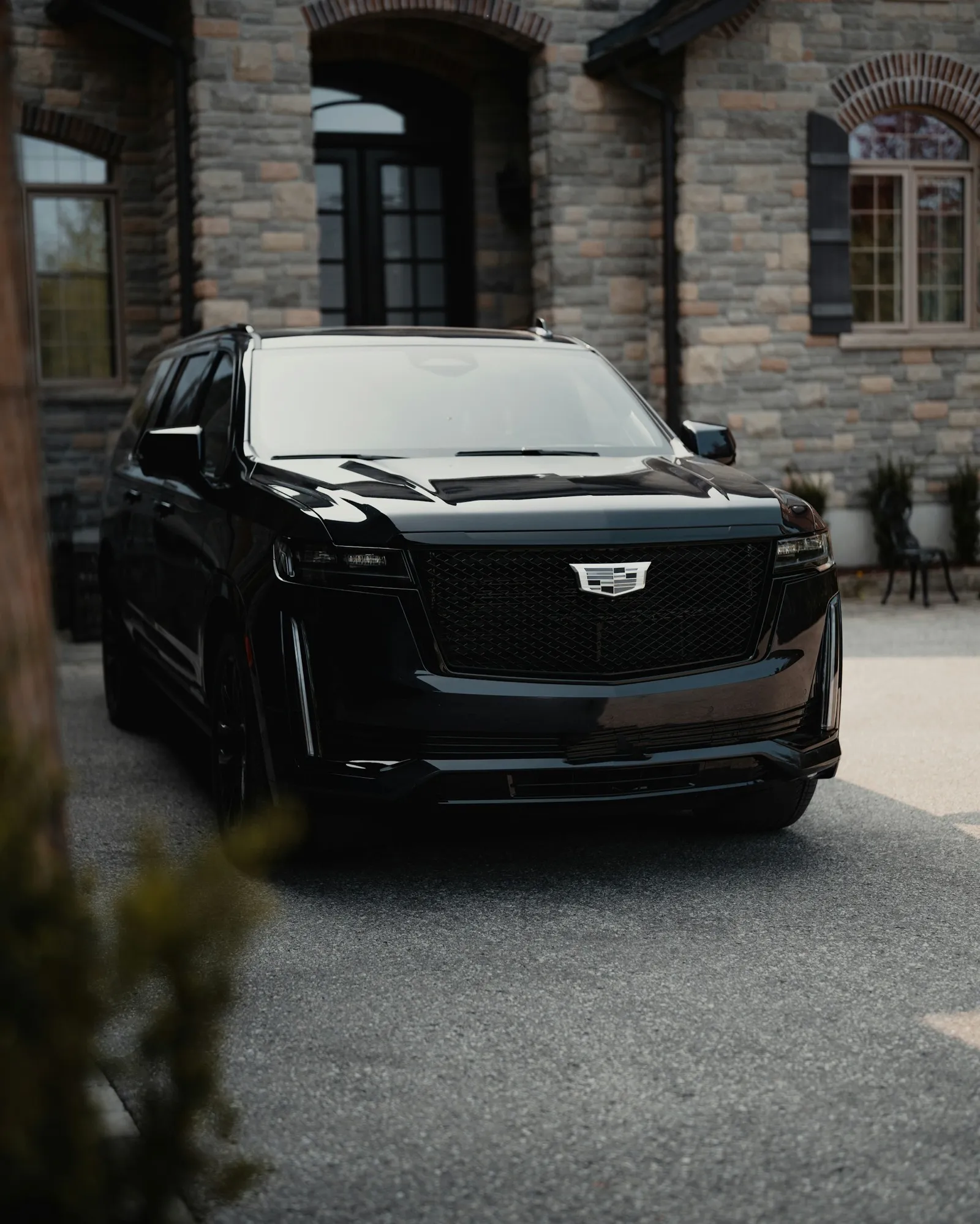 Black Cadillac Escalade parked in front of a stone mansion
